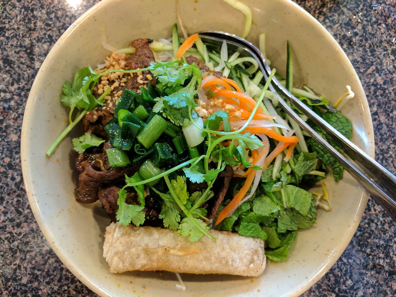 A vermicelli bowl at Dong Que, under a shower of herbs and a crisply fried spring roll, makes a satisfying one-bowl meal.