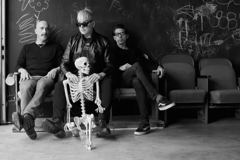Image: The band members of Alkaline Trio pose with a skeleton in a black and white press photo.