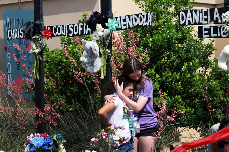 Image: Emma Hampton (R) comforts a child as she visits a cross that bears the name of her best friend at the memorial set up at the Allen Premium Outlets mall.