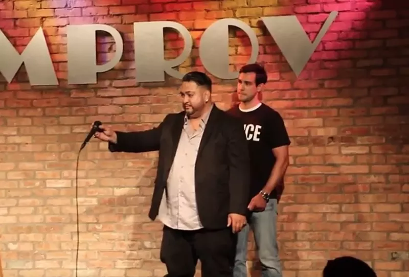 Image: Comedian George Redd prepares to assume the position as a "police officer" takes him into custody.