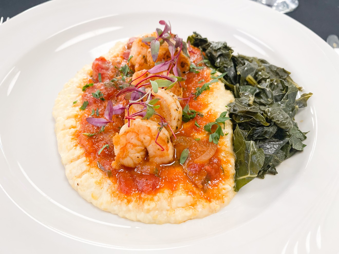 A typical meal that includes shrimp and grits served with a light tomato sauce and a side of braised collard greens.