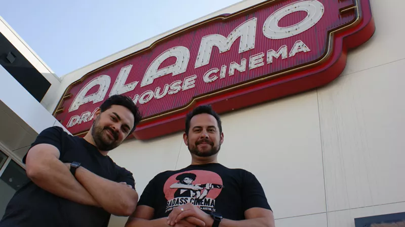 Image: Alamo Drafthouse DFW creative director James Wallace (left) and chief operating officer Bill DiGaetano stand in front of the 20-by-40-foot neon sign for the chain's newest movie theater in the Toyota Music Factory in Irving.