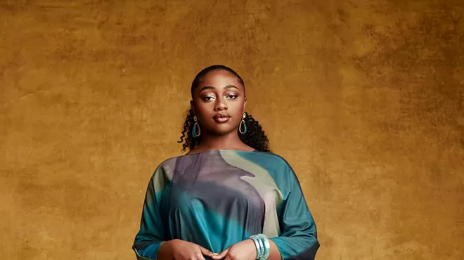 A woman standing in front of orange background.