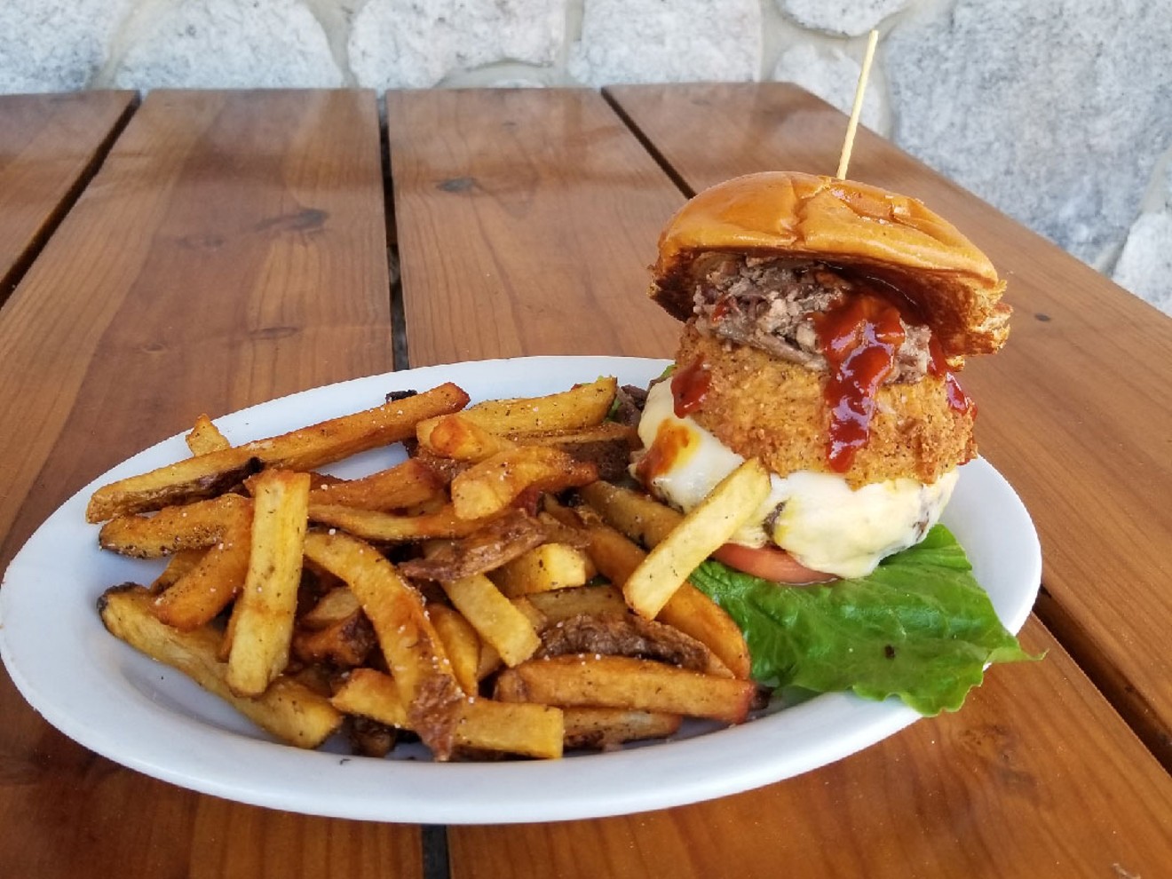 The Elvis cheeseburger is a smoked patty topped with provolone and American cheese, plus a huge onion ring filled with chopped brisket and topped with BBQ sauce, Romaine lettuce and tomato on a challah bun ($14.99).