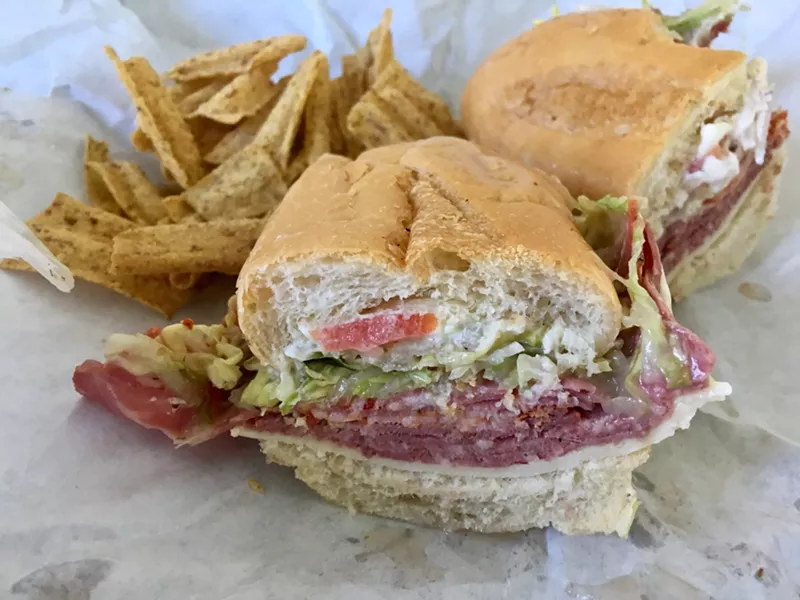 Image: A ham, cheese and capicola sandwich with shredded lettuce, tomato and sheer-thin onion on a white Village Bakery bun.