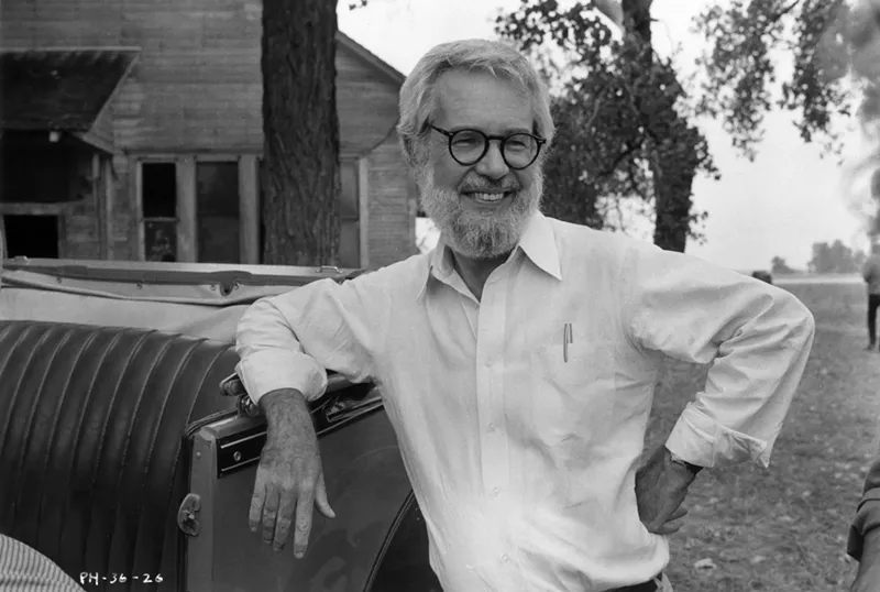Image: 1984: Robert Benton, leaning against a vintage car and smiling in front of a wooden house on the set of his film, Places in the Heart.