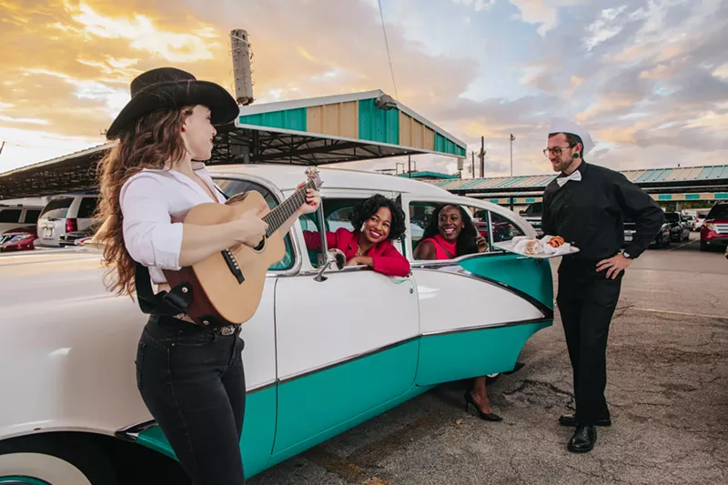 Image: Entertainment for a COVID world. Taylor Shead and Olivia Taylor listen to Ashley Whitby play guitar while being served food by Casey Reid at Keller's drive in. Vintage car owned by Lindel.