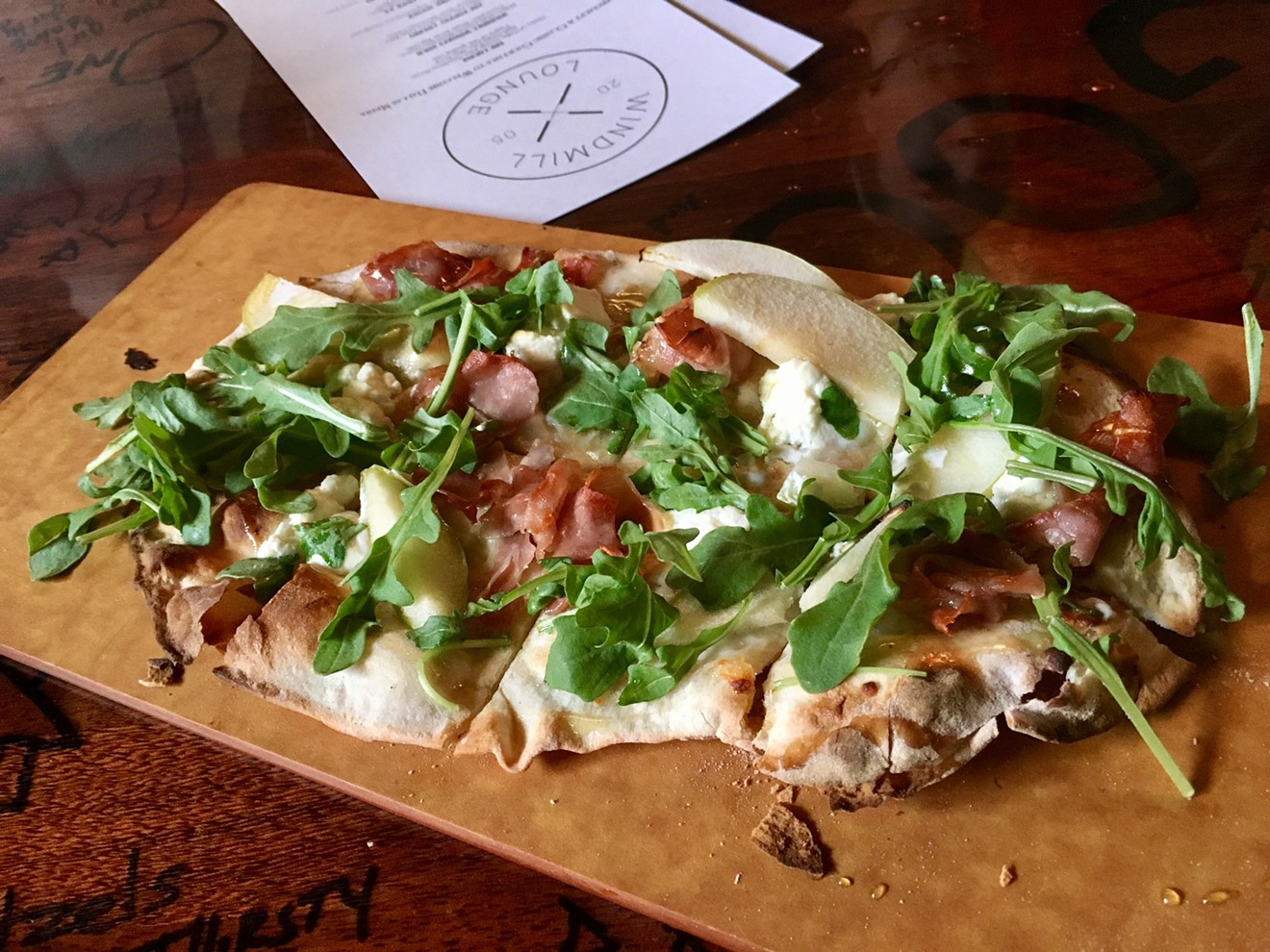 One of the new flatbreads at the Windmill Lounge has prosciutto, apples, goat cheese, arugula and garlic oil.
