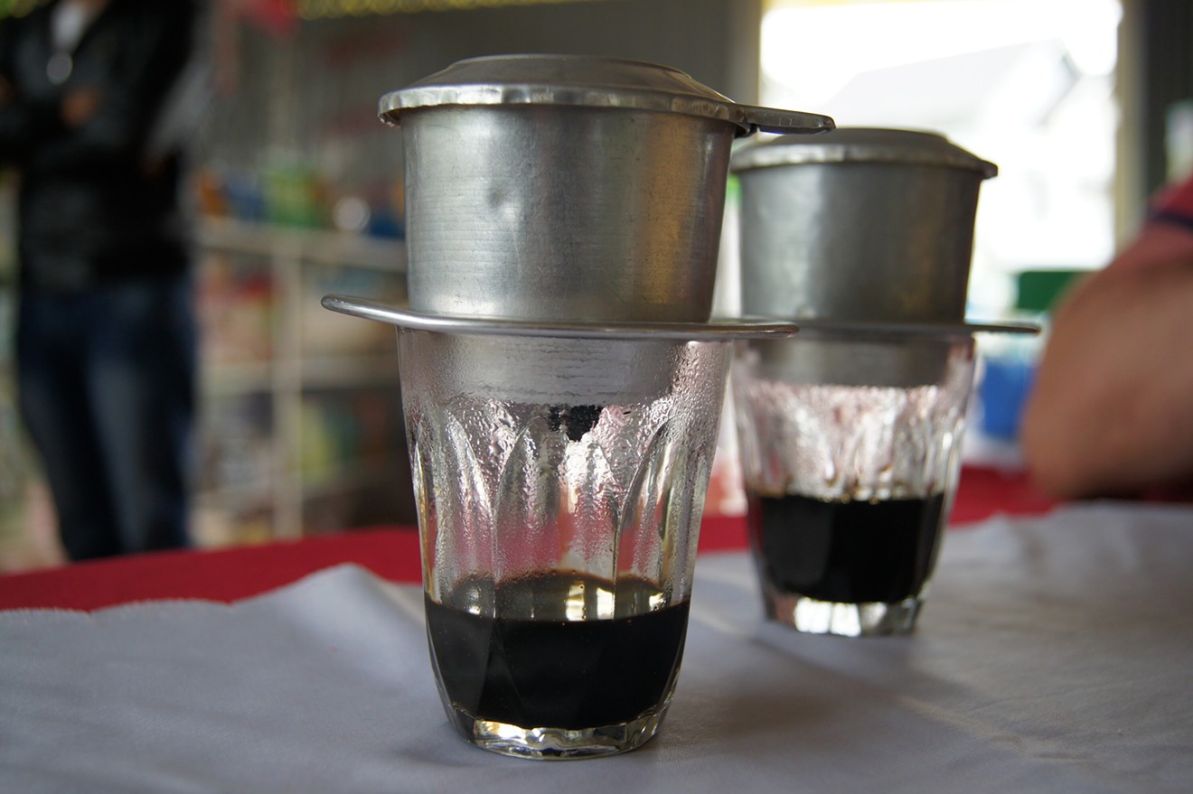 A phin filter, seen here, sits on top of a coffee cup. Typically a strong brew is poured through, then condensed milk is added.