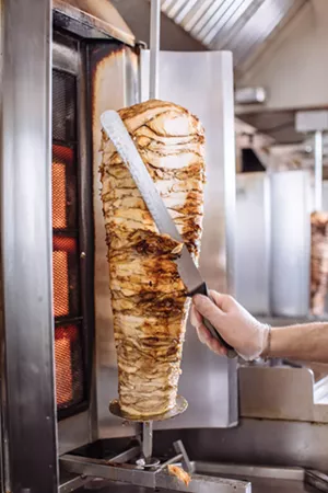 The beef and chicken for shawarma are sliced thinly and then loaded onto a vertical rotisserie spit in a massive stack of meat. As the spit turns, a thin layer is shaved off each time a customer orders. - KATHY TRAN