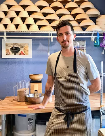 Room rater: 10/10. Tattoo on arm serves as plant, natural lighting, peaceful lavender wall color, nice art, bowls are cool and milling your own flour covers everything else. - PHOTO COURTESY OF TYLER ROONEY
