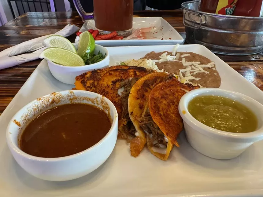 A plate of birria tacos with consommé sauce, refried beans and rice.