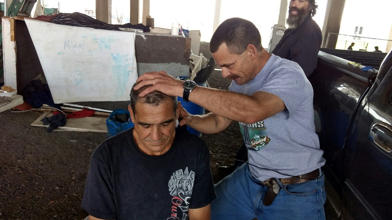 Robert, right, trims the back of Eutemio's neck using electricity borrowed from a  visitor's truck in the homeless encampment beneath Interstate 30 near Fair Park.