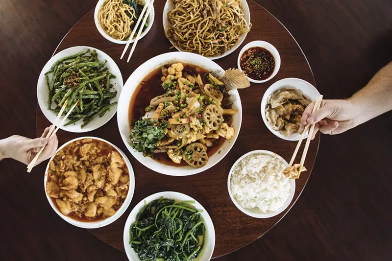 Image: Center: the whole fish with cauliflower, potatoes, and lotus root; Clockwise from top: beef lo mein, Chengdu dumplings, water spinach, fish fillets and bamboo shoots in spicy chili sauce topped with serrano, sauteed string beans, dan dan noodles.